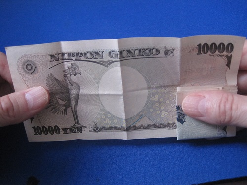 一万円札をひろげます。同時に、裏側の千円札は親指で押さえておきます