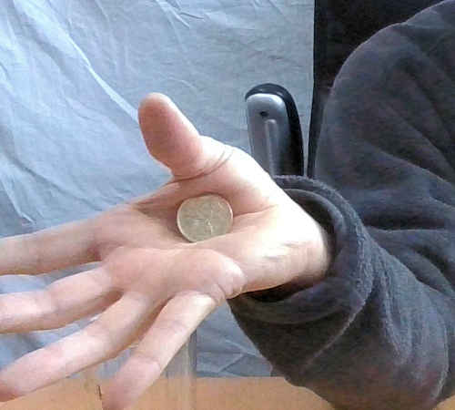 右の手でパームをしてコインを保持している