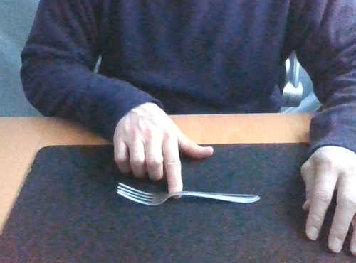 フォークをテーブルに置き、右手の人差し指を付け根に入れて曲がり具合を示します