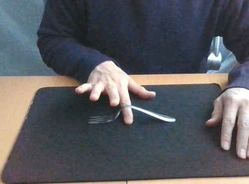 フォークをテーブルに置き右手の人差し指を付け根に入れて曲がり具合を示します