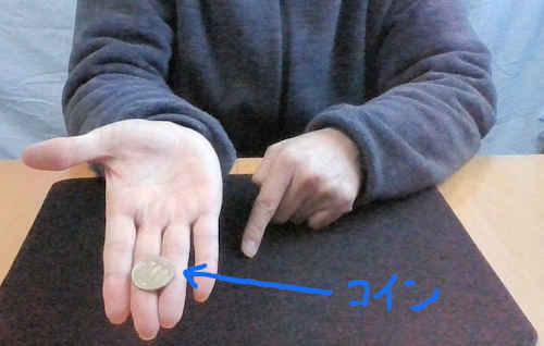 右手の中指と薬指の第一関節と第二関節の間にコインをおきます