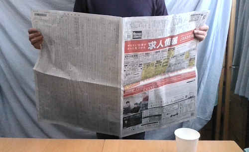 新聞紙を両手に持ち、ひろげて見せます